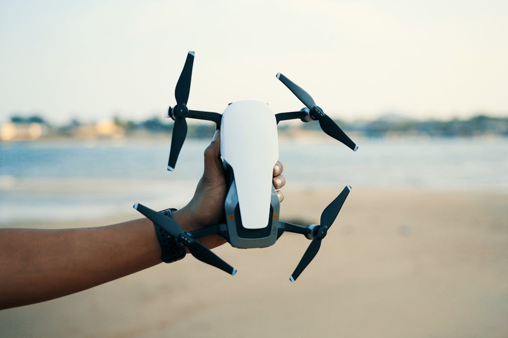 Close-up of a hand holding a drone on a beach during daytime, showcasing modern technology.